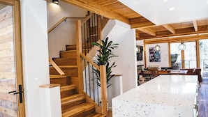 A wooden staircase with a glass railing, a kitchen area with a large island, and a dining space with wooden furniture.
