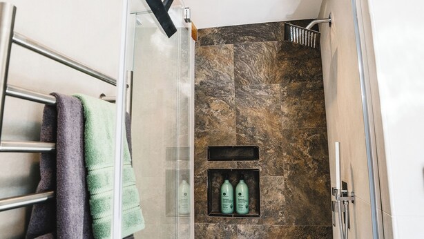 A modern bathroom with a glass shower enclosure, a towel rack with multiple towels, and a shelf with two bottles of shampoo. - Taos Ski Hut - Modern Mountain Magic (Taos Ski Valley)