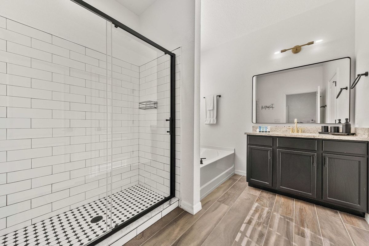 Un baño moderno con ducha envuelta en vidrio, bañera y tocador con muebles oscuros.