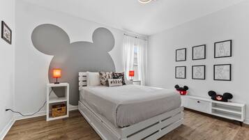 Une chambre à coucher avec un lit, une table de chevet, une lampe, une décoration murale à l’effigie de Mickey Mouse et des tableaux encadrés accrochés au mur.