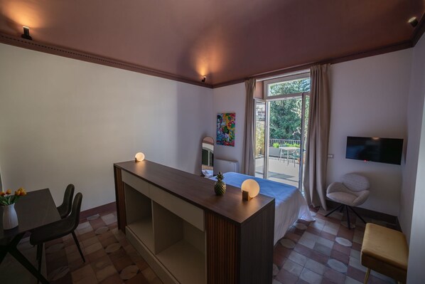 Una habitación de hotel moderna con un escritorio de madera, una cama, un televisor y un balcón con vistas al exterior.