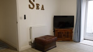 Ein Wohnzimmer mit Fernseher, einem Holzschrank und einem braunen Ledersitzhocker.