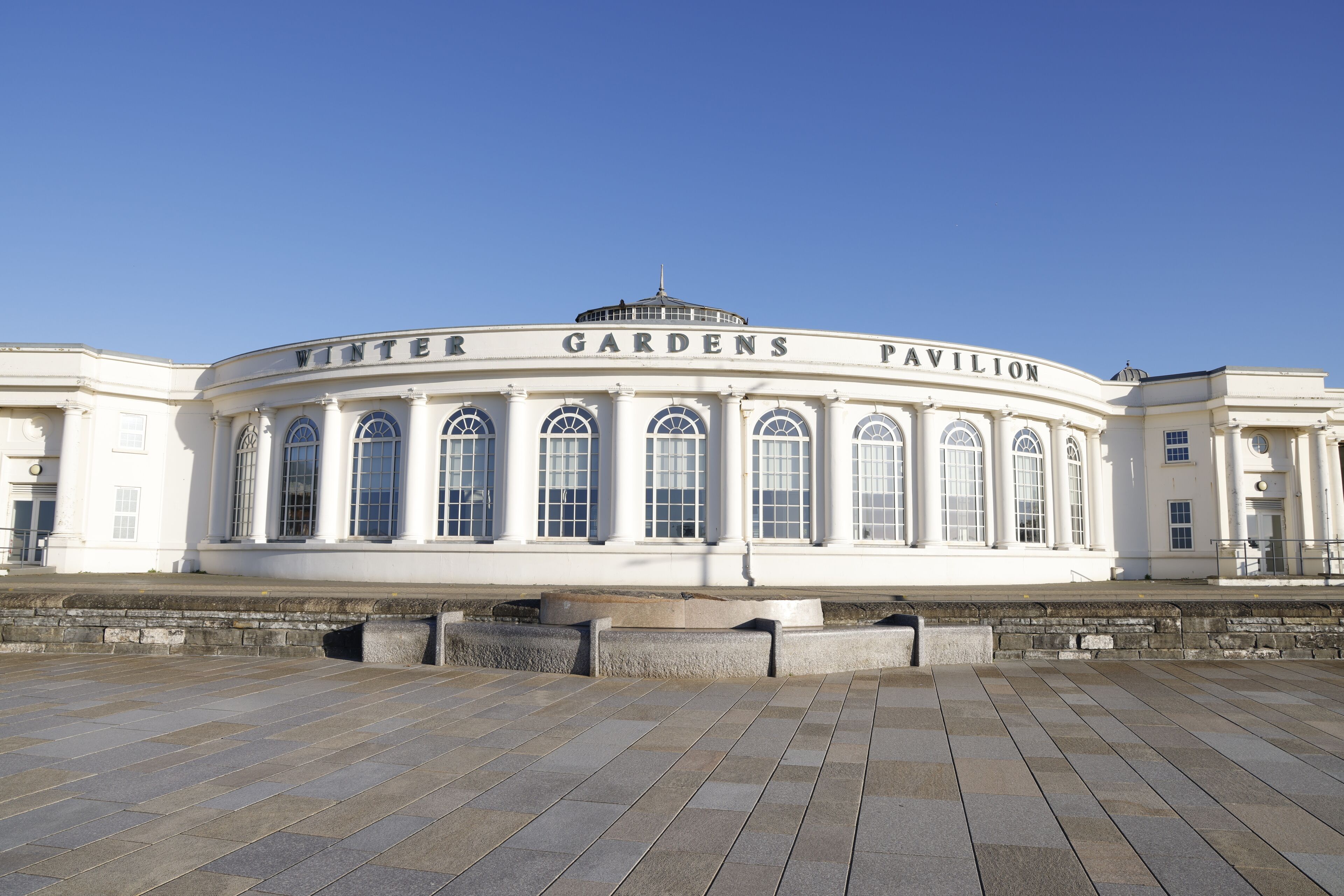 Un bâtiment blanc doté de fenêtres en arc de cercle, sur la façade duquel on peut lire les mots « Winter Gardens Pavilion ».