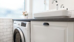 A modern laundry room with a front-loading washing machine, a sink, and a window with frosted glass. - Ideal Remote Workspace + Quiet + Great location (Brighton and Hove)