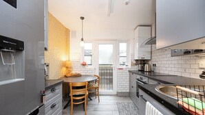A modern kitchen with a stainless steel refrigerator, a water dispenser, a wooden dining table with chairs, a black countertop, and a window with a view of the outside. - Ideal Remote Workspace + Quiet + Great location (Brighton and Hove)