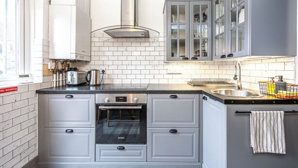 A modern kitchen with white cabinets, a built-in oven, a stainless steel range hood, and a window providing natural light. - Ideal Remote Workspace + Quiet + Great location (Brighton and Hove)