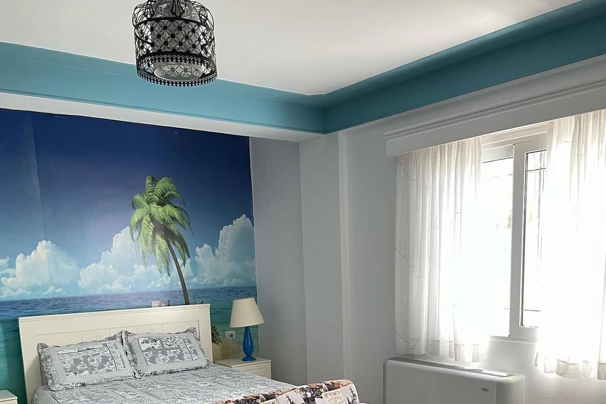 Une chambre à coucher comprenant un lit, un canapé, une table basse, une table de chevet, une lampe, une décoration murale et une fenêtre avec des rideaux.
