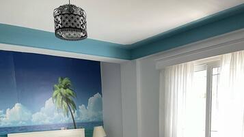 Une chambre à coucher comprenant un lit, un canapé, une table basse, une table de chevet, une lampe, une décoration murale et une fenêtre avec des rideaux.