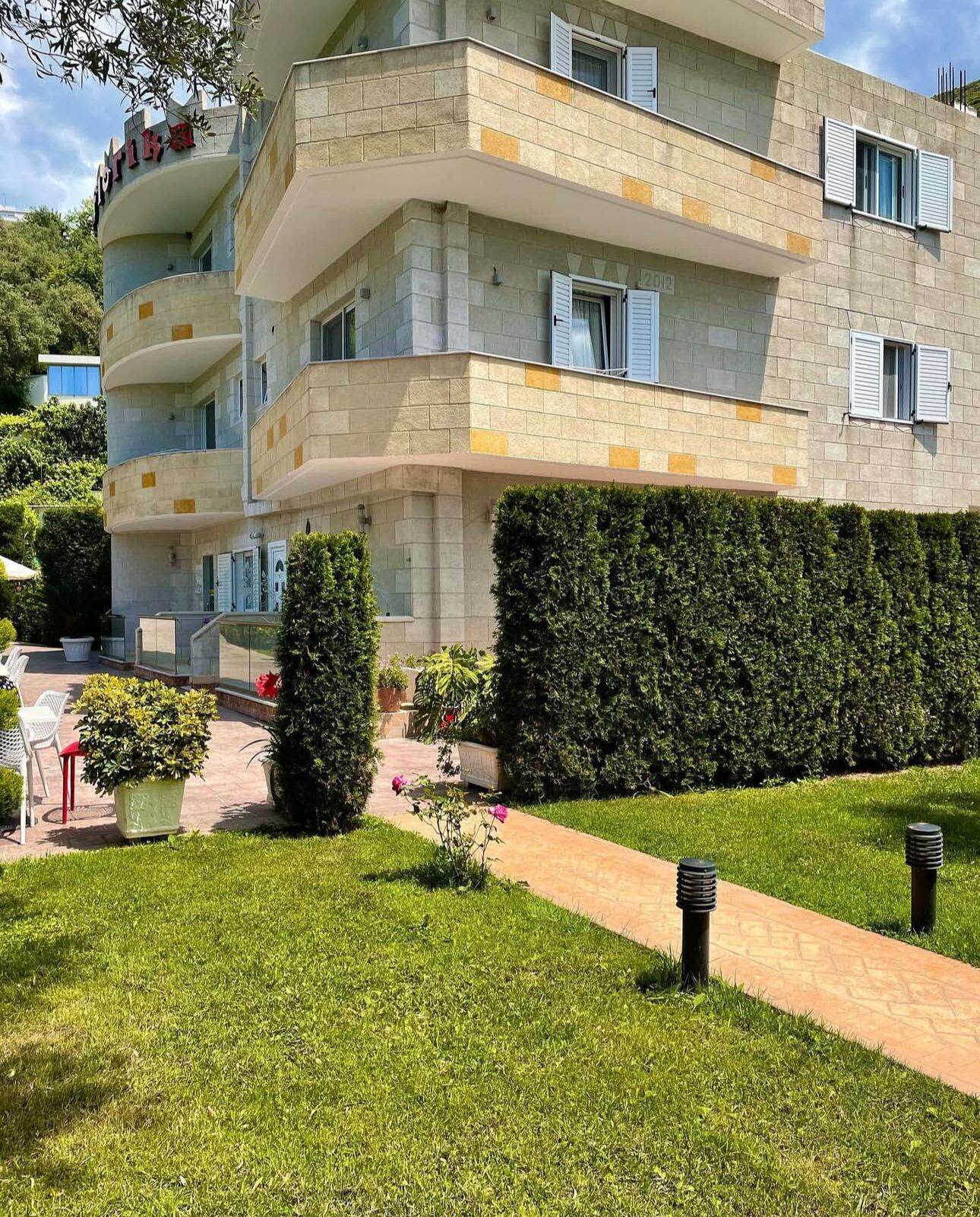 Un edificio de varios pisos con fachada de piedra, balcones y un jardín bien cuidado con un sendero.