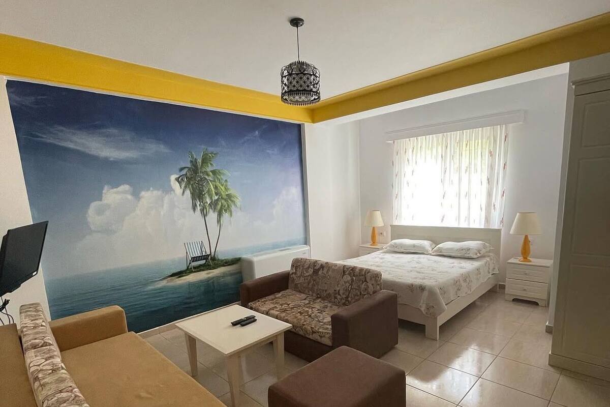 Une chambre d’hôtel avec un lit, un canapé, une petite table et un tableau représentant une scène de plage.