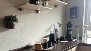 A kitchen with wooden cabinets, a dark countertop, a coffee maker, a kettle, and a small potted plant. - Vacation apartment RIVA (Kronau)