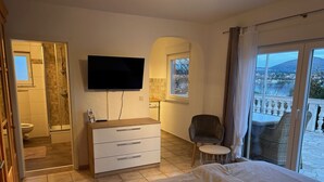 A bedroom with a bed, a TV, a desk, and a chair. There is a bathroom visible through an open door. - Cozy apartment for 2 pers with all amenities, 50 meters from the lake (Bilice)