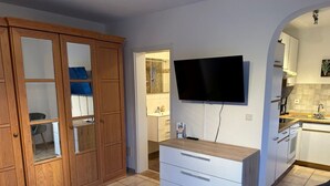 A bedroom with a wooden wardrobe, a TV mounted on the wall, and a kitchen area with a sink and stove. - Cozy apartment for 2 pers with all amenities, 50 meters from the lake (Bilice)