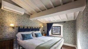 A bedroom with a bed, a nightstand, an air conditioning unit, a window with curtains, and a view of the outside. - Pitti Art by MMega Homes and Villas (Florence)