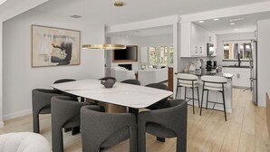 Une cuisine moderne avec des meubles blancs, un coin repas doté d’une table en marbre et de chaises recouvertes d’un tissu gris.