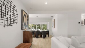 Un salon moderne avec un canapé blanc, un banc en bois et un coin repas comprenant une table et des chaises.