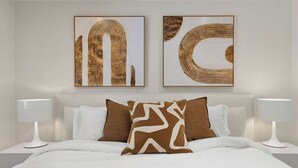 Une chambre à coucher avec un lit, deux lampes de chevet et deux tableaux abstraits accrochés au mur.