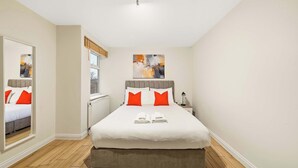 Un lit bien fait, avec une literie blanche et rouge, une lampe de chevet et des œuvres d’art accrochées au mur.