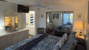 Ein Schlafzimmer mit einem großen Bett, einem Schreibtisch, einem Stuhl, einem Spiegel und einem Deckenventilator.