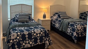 Ein Schlafzimmer mit zwei Betten, einem Deckenventilator, einem Nachttisch mit Lampe und einem Fenster mit Jalousien.