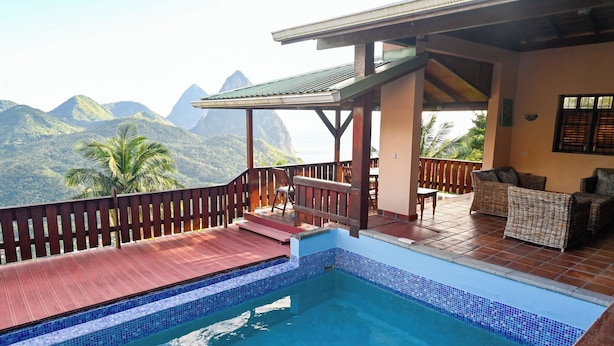 Un área de piscina con vistas a montañas, una terraza cubierta con muebles de mimbre y una barandilla de madera.