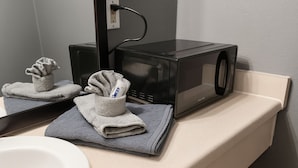 A bathroom with a black microwave on the counter, a towel rack with folded towels, and a mirror reflecting the microwave. - 107 Gated King Bed Hotel Room (Jackson)