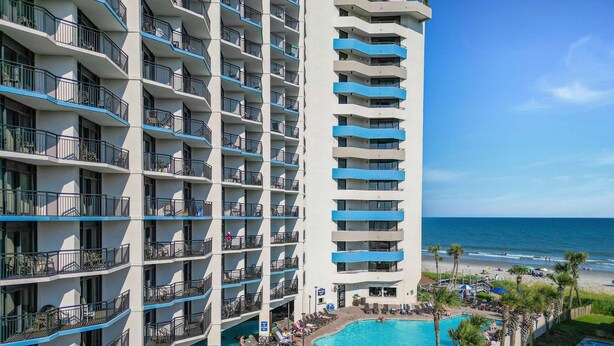 A multi-story hotel with balconies, a pool area with umbrellas, and a view of the beach. - 💎Oceanfront | Amazing Views | Relax in Luxury | Ocean Reef Resort 818💎 (Myrtle Beach)
