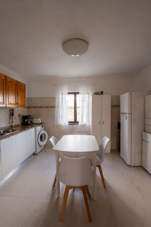 A compact kitchen with a dining table, washing machine, and a refrigerator.