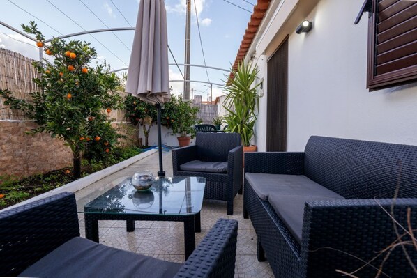 A patio with wicker furniture, a glass table, and potted plants.