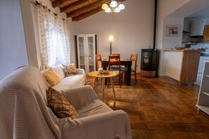A cozy living room with a sofa, a dining table with chairs, a small round table with a lamp, and a kitchen area with a stove.