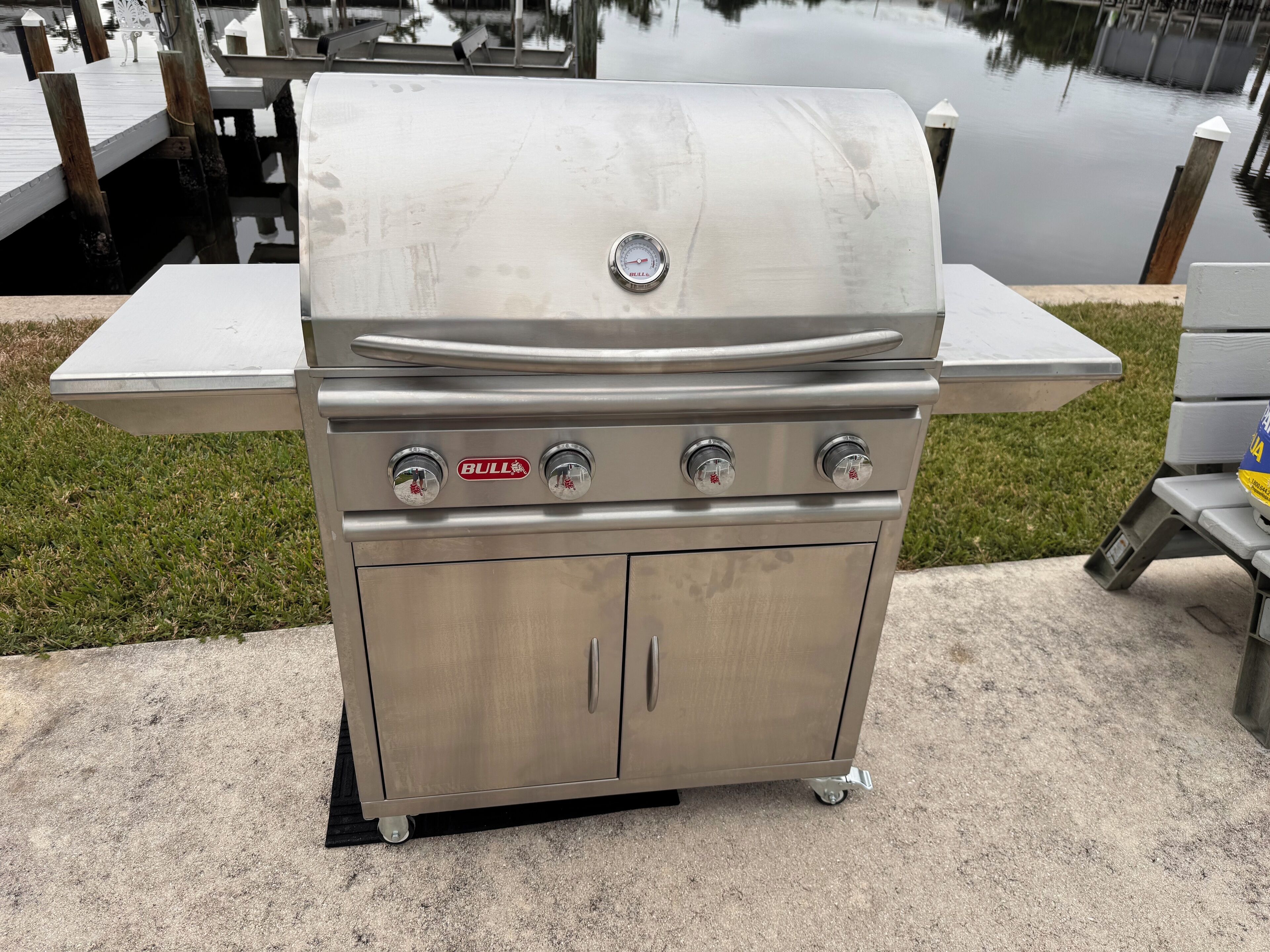 Ein Grill aus Edelstahl mit Beistelltisch und Schrank, in der Nähe von Wasser gelegen.