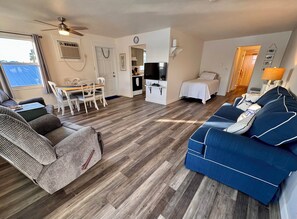 Een woonkamer met een bank, een eettafel met stoelen, een televisie en een bed.
