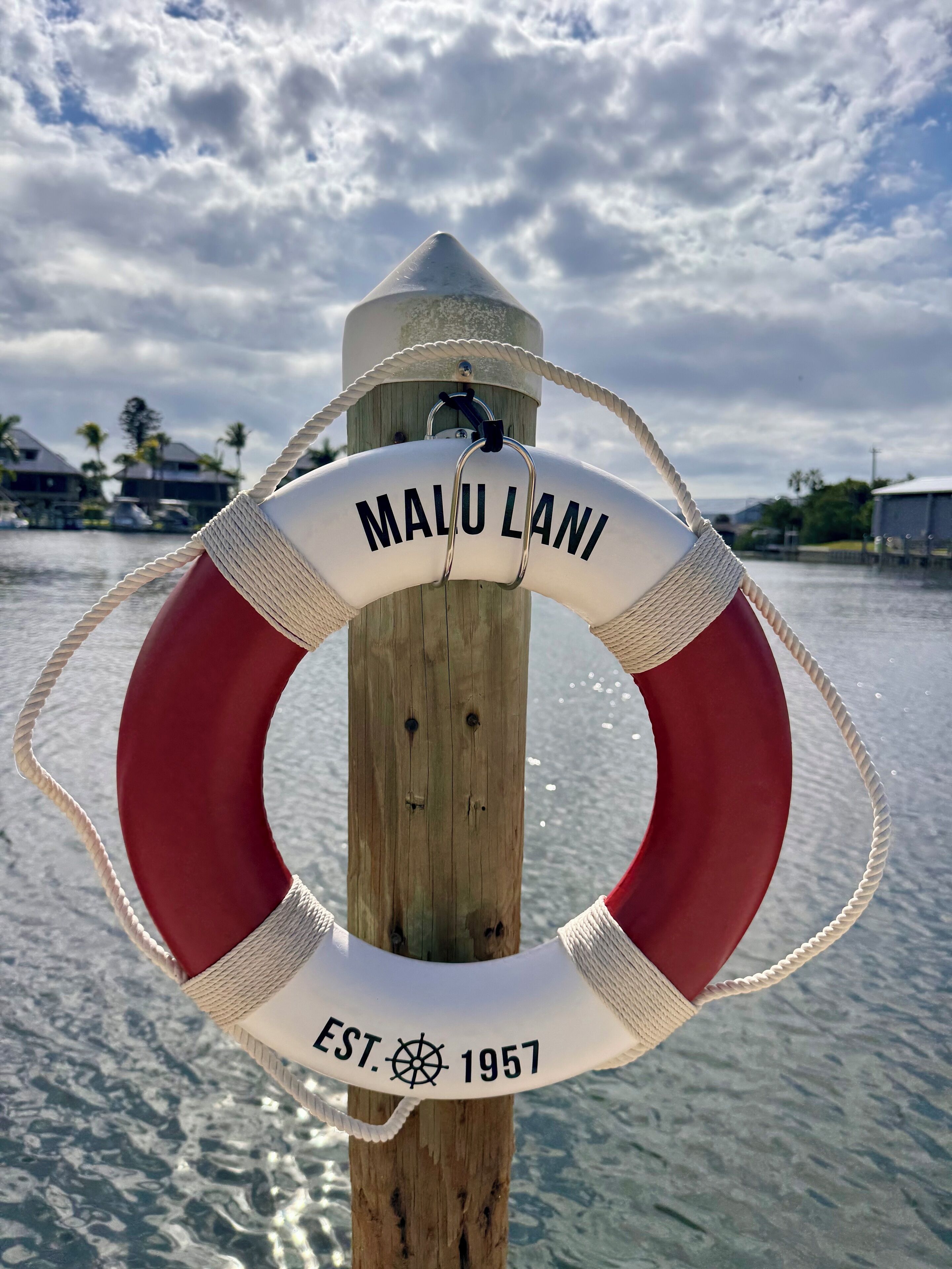 Una boya con el texto "MALU LANI" y "EST. 1957", sujeta a un poste de madera con una cuerda.