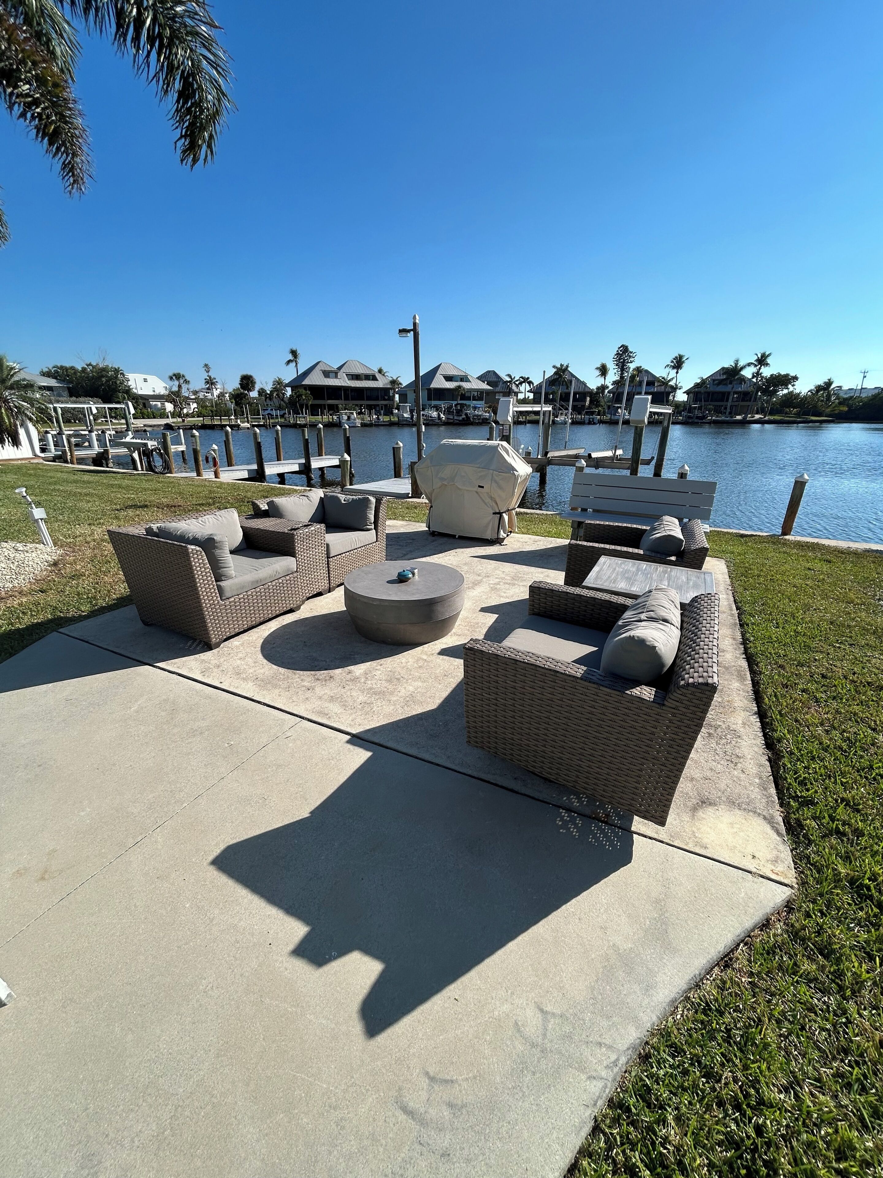 A waterfront patio with outdoor furniture, a grill, and a view of the marina and buildings in the background.