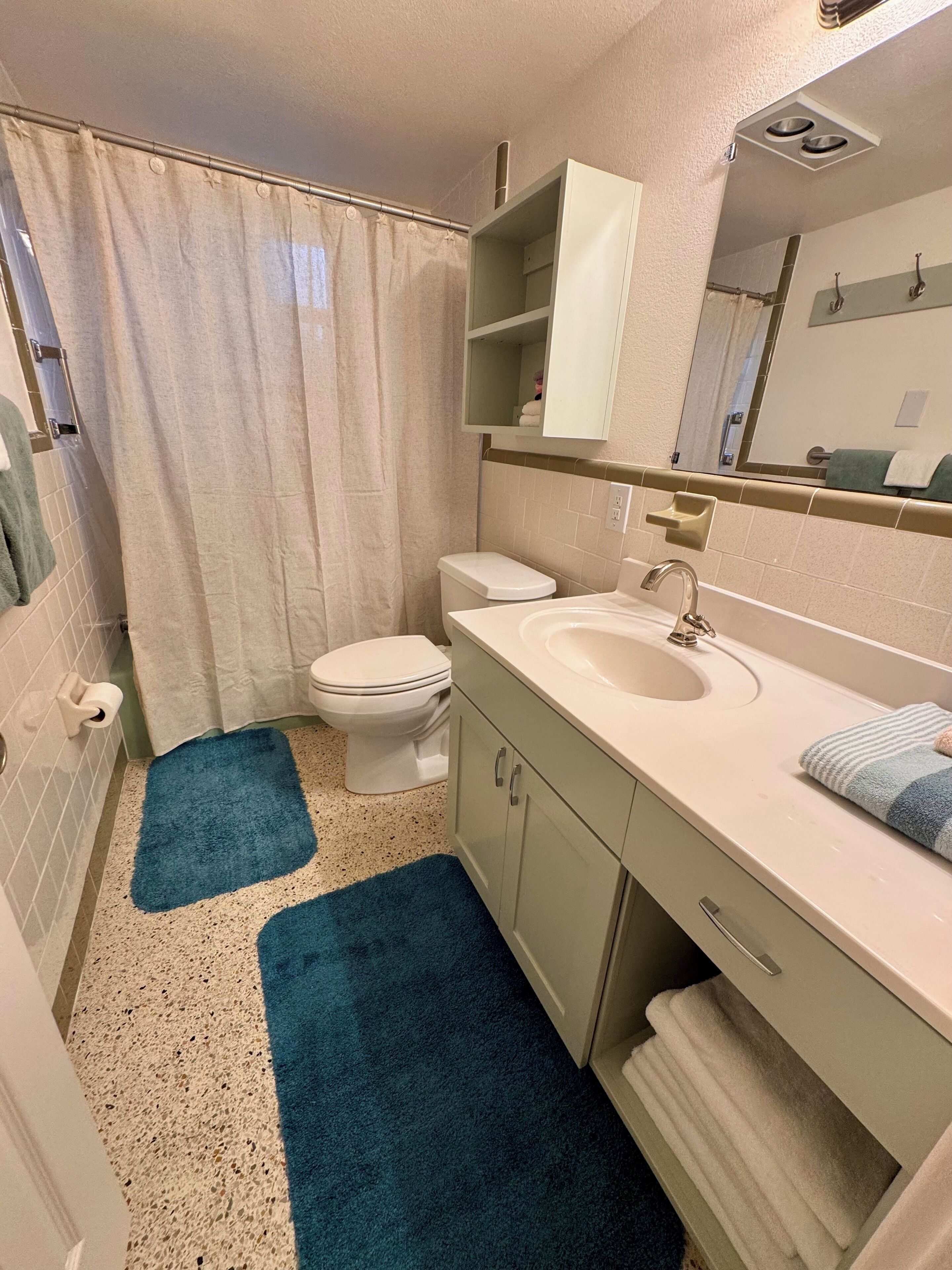 A bathroom with a toilet, sink, and mirror. There is a shower curtain and a blue rug.