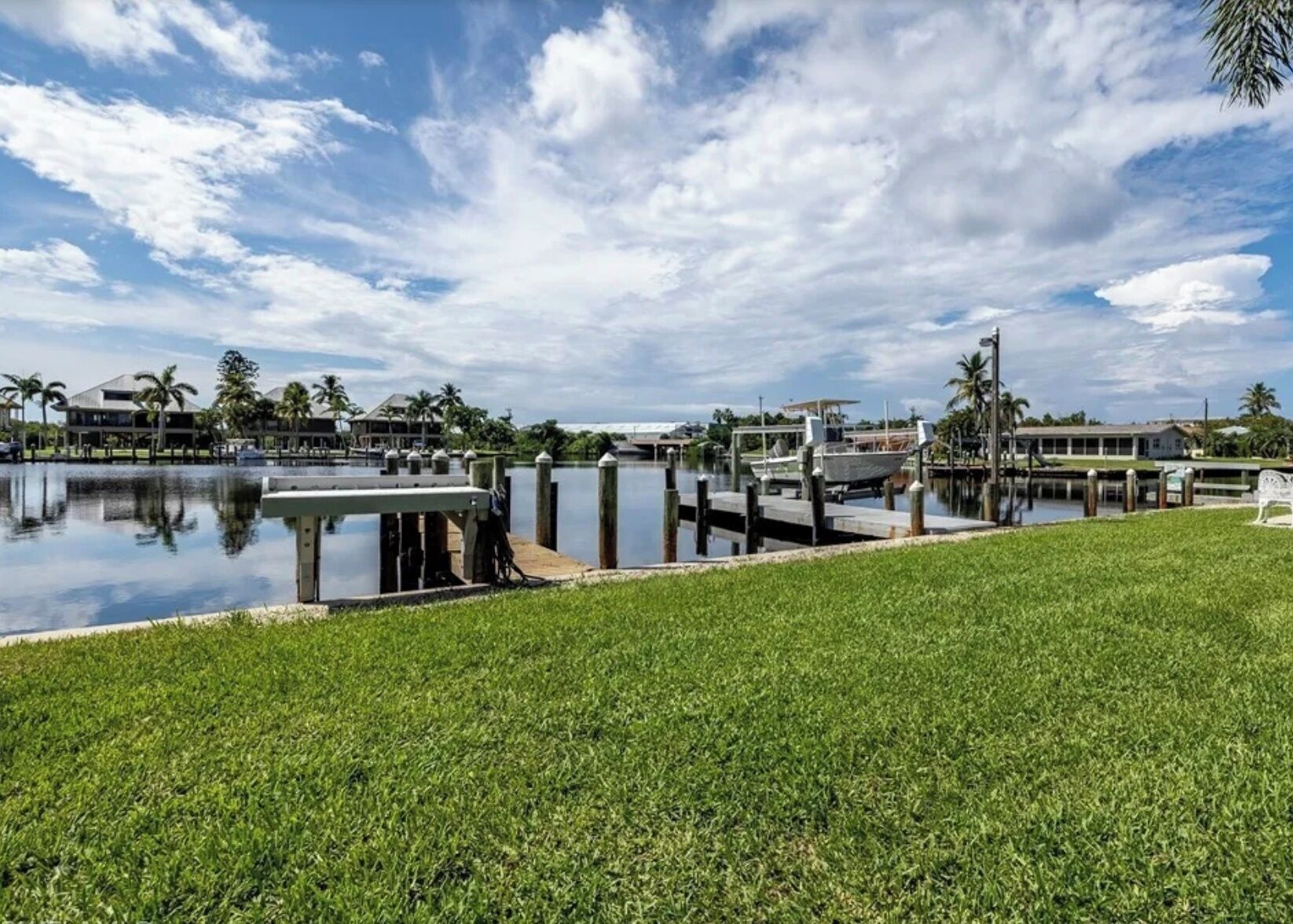 A marina with boats docked, a grassy area in the foreground, and buildings in the background.