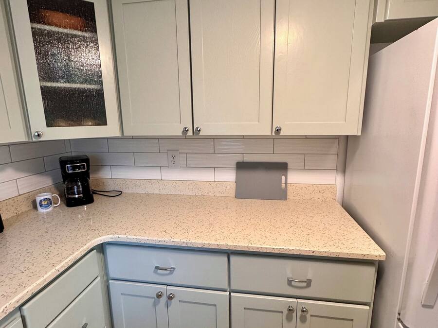 A kitchen with light green cabinets, a speckled countertop, and a coffee maker.