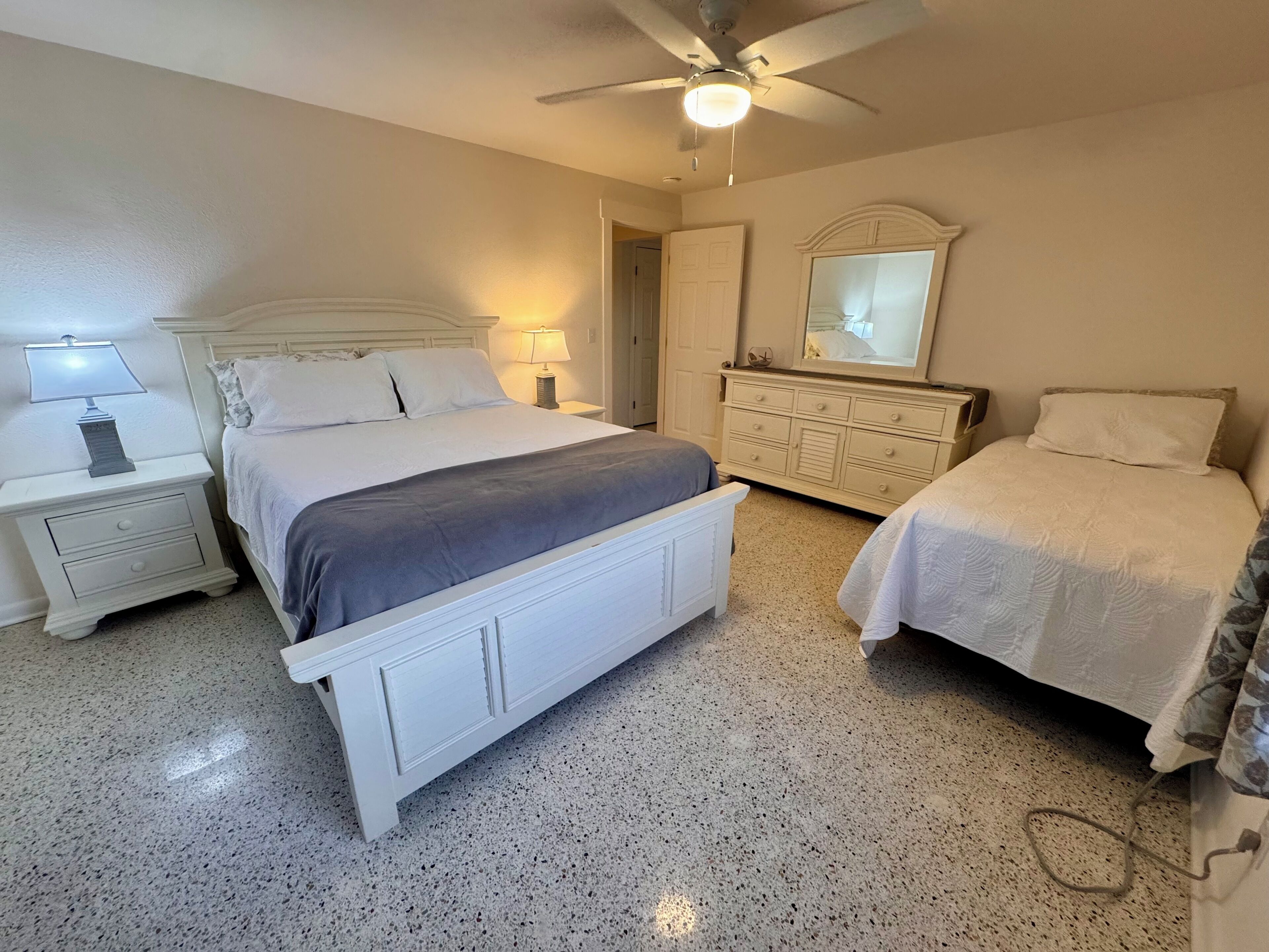 A bedroom with a large bed, two bedside tables, a dresser, a ceiling fan, and a mirror.