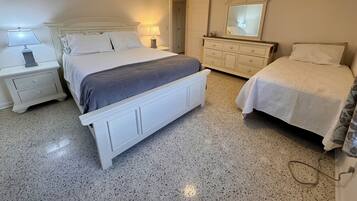 A bedroom with a large bed, two bedside tables, a dresser, a ceiling fan, and a mirror.