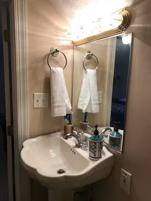 Un baño con lavamanos blanco, dos toalleros, un espejo y una luz encima del espejo.