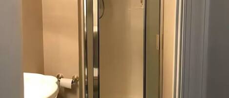A small bathroom with a toilet, a shower stall, and a sink.