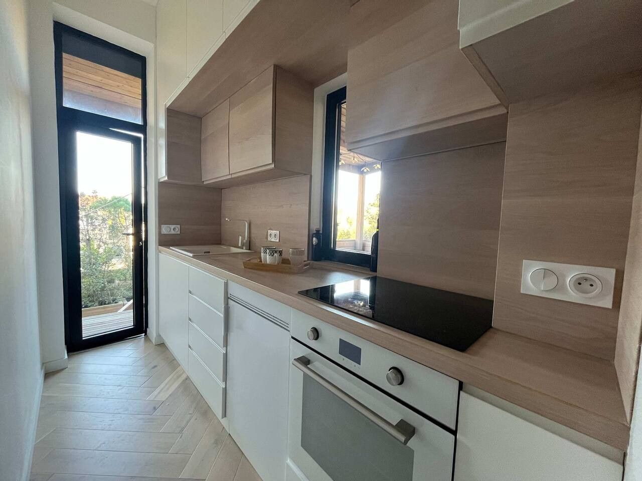 Une cuisine moderne dotée d’un four encastré, d’une fenêtre au-dessus de l’évier et d’une porte donnant sur un espace extérieur.