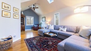 A modern living room with a grey sectional sofa, a patterned rug, and a ceiling fan. - Charming 3-bedroom house with AC in peaceful Tiverton (Tiverton)