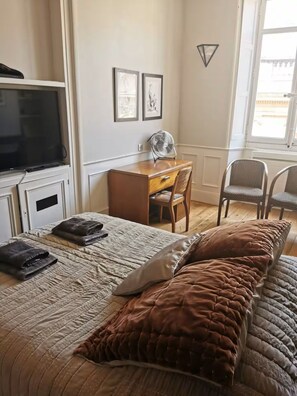 Une chambre à coucher avec un lit, un bureau, une chaise, une télévision et une fenêtre.