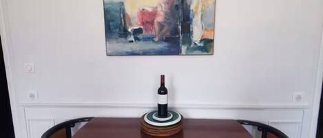 A dining table with a wine bottle centerpiece, flanked by chairs, in a room with a large abstract painting on the wall.