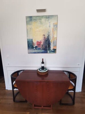 A dining table with a wine bottle centerpiece, flanked by chairs, in a room with a large abstract painting on the wall. - Charming Bordeaux Apartment: 2 Bedrooms, Free Park (Bordeaux)