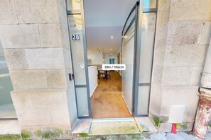 Entrada de hotel com o número '30' na parede, porta de vidro e corredor com carpete que leva a um quarto.