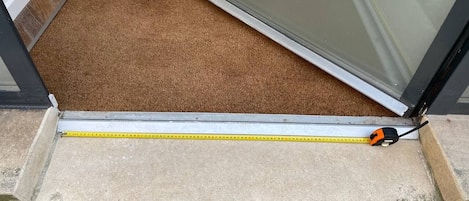 A measuring tape across a threshold with a brown carpet and a glass door.