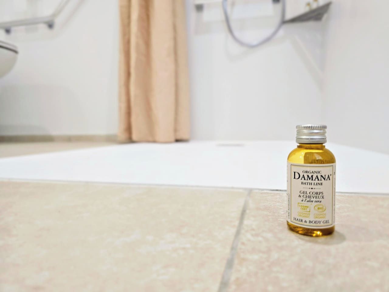 Ett badrum med badkar, dusch och en flaska med ekologiska produkter från Damanas badsortiment som står på golvet.