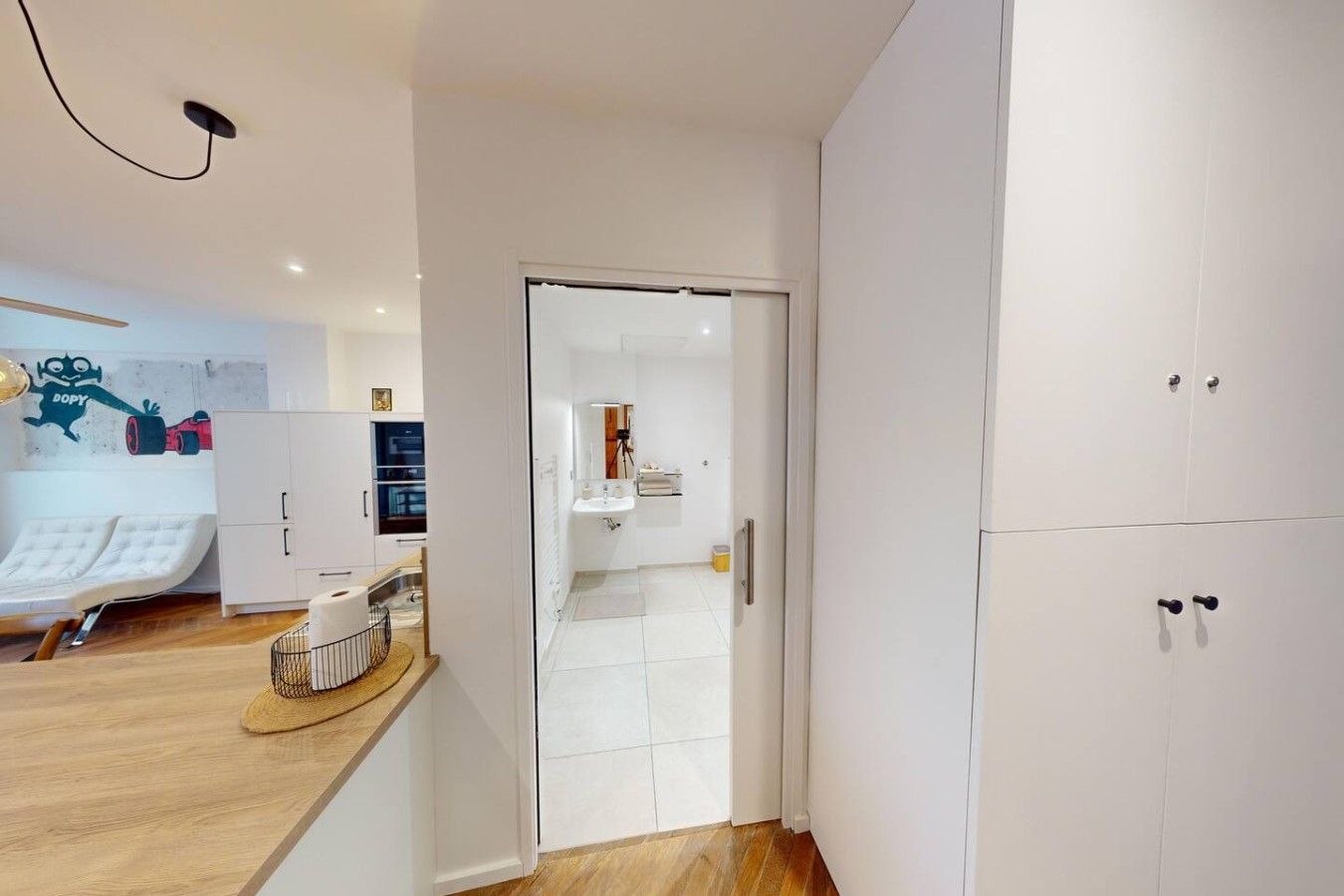 Un interno moderno con un armadio bianco, un lavandino bianco e un pavimento in legno.